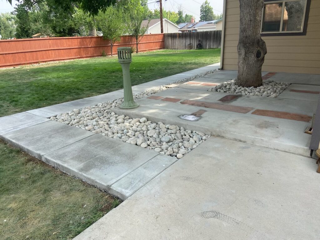 Concrete backyard patio with rock borders around a mature tree