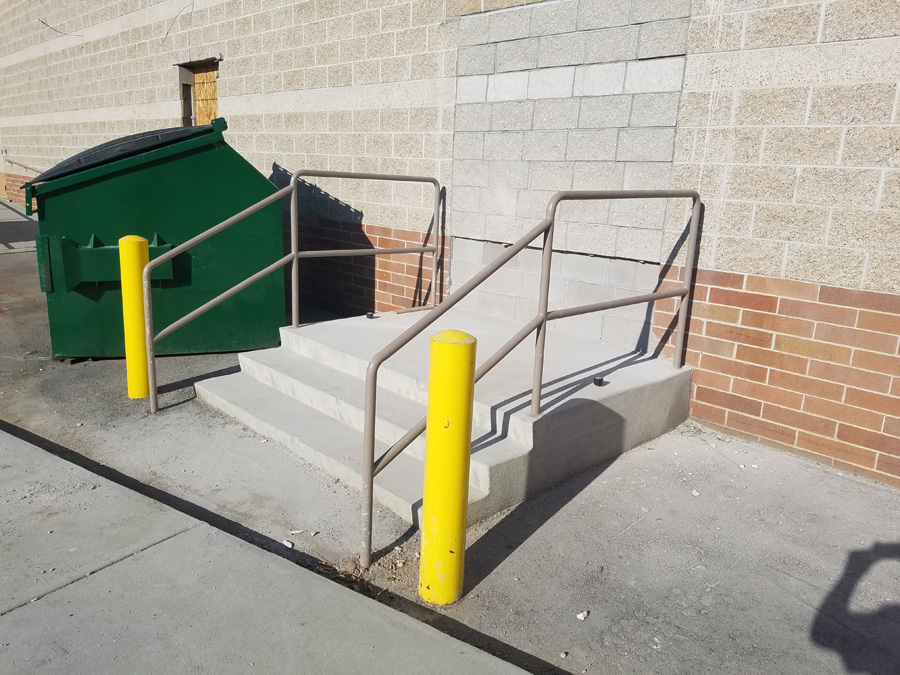 Concrete service-entry steps with metal handrails beside a commercial building