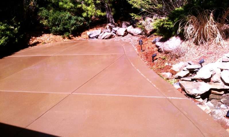 Warm-colored concrete patio with control joints beside a landscaped garden