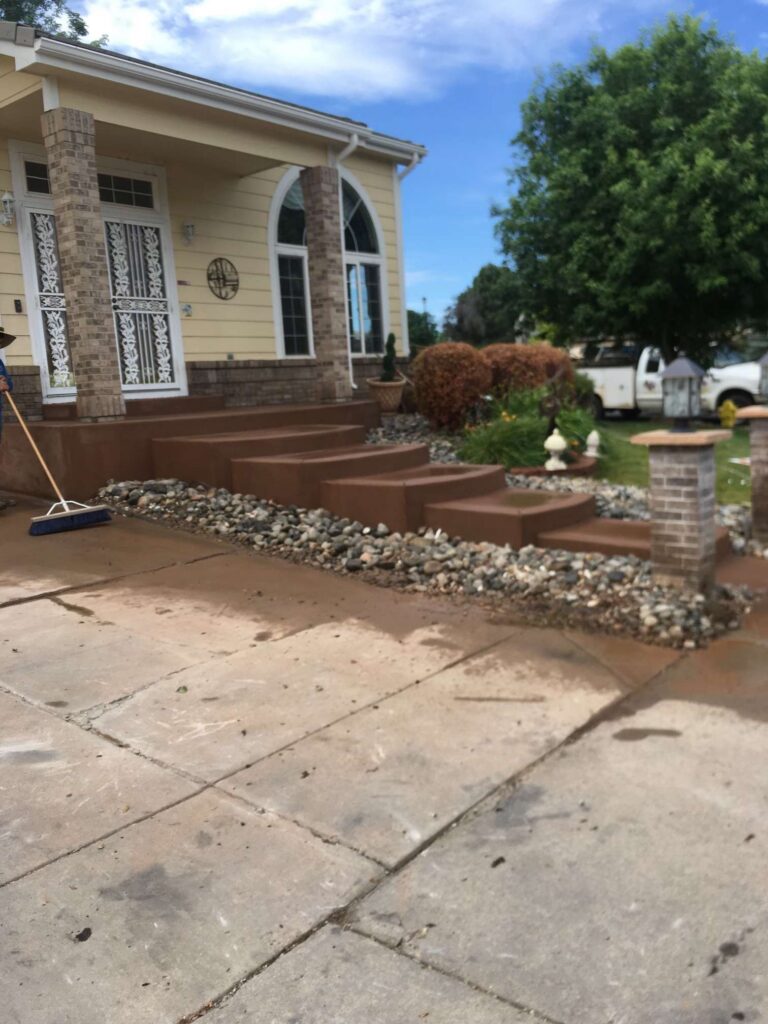 Colored concrete walkway leading to a home entrance and garden