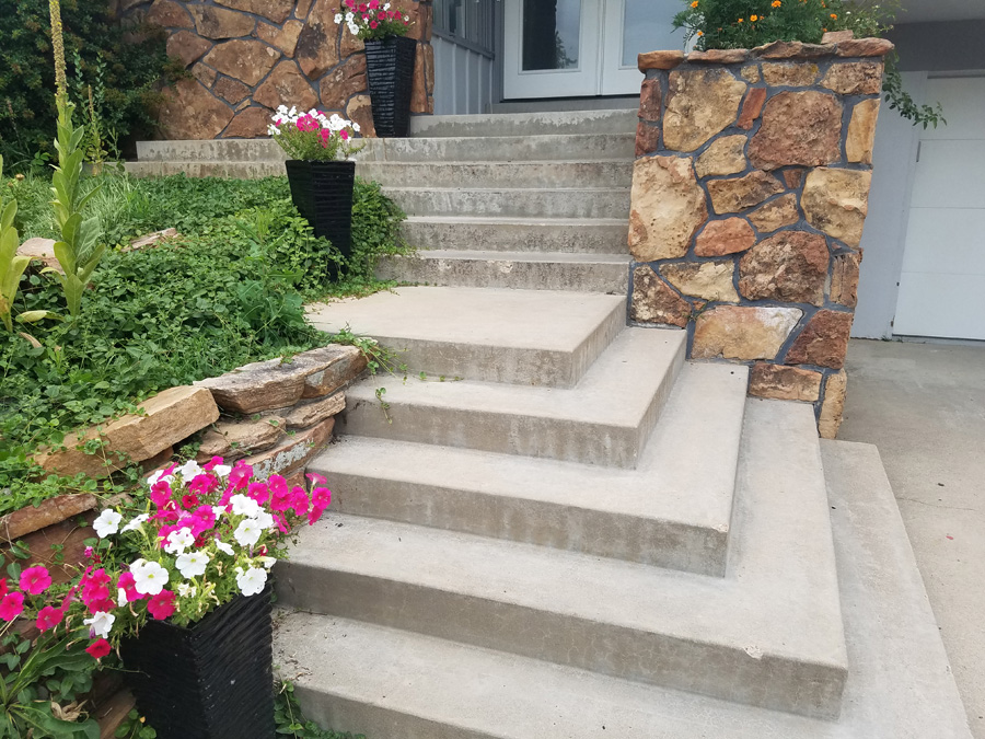 Concrete entry steps between stone columns and garden beds