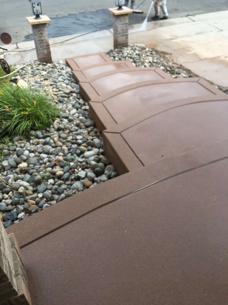 Curved colored concrete walkway beside a landscaped front garden
